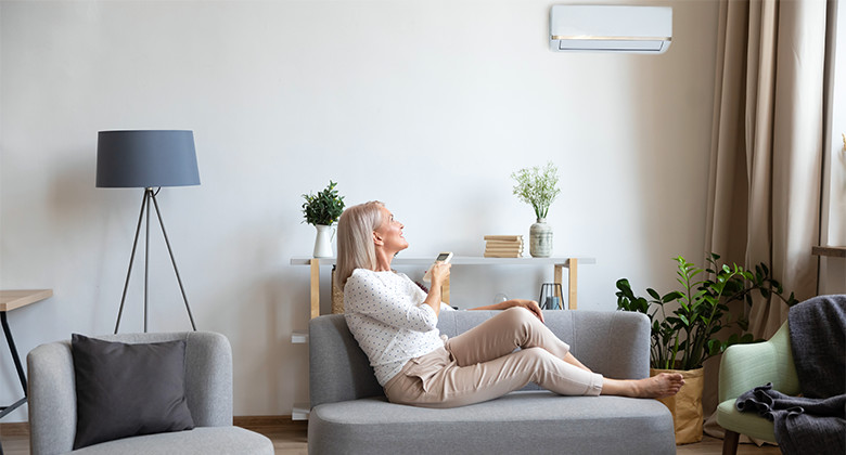 Woman Controlling Air Source Heat Pump from Couch with Remote